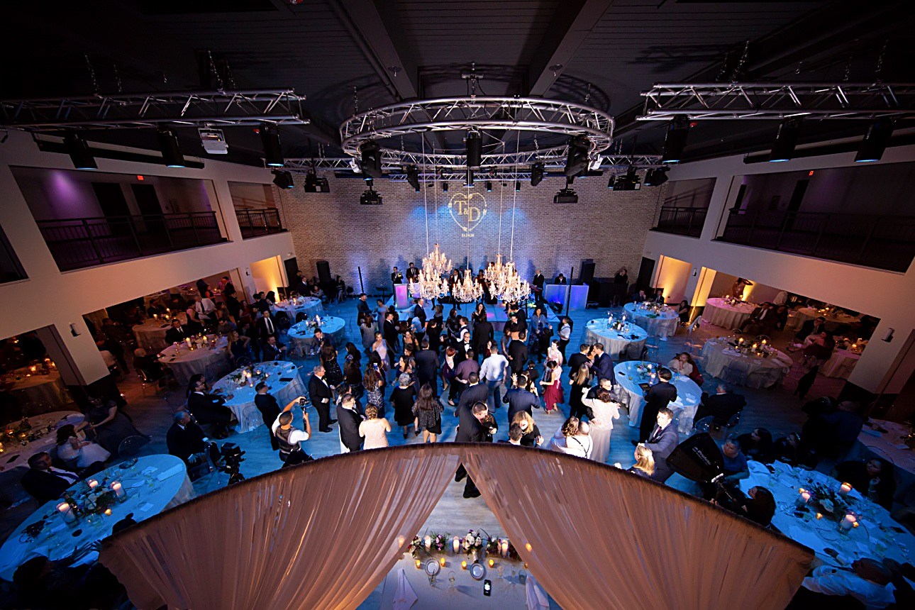 Un salón de eventos en plena celebración: pista de baile, arañas de cristal y mesas redondas vistas desde arriba