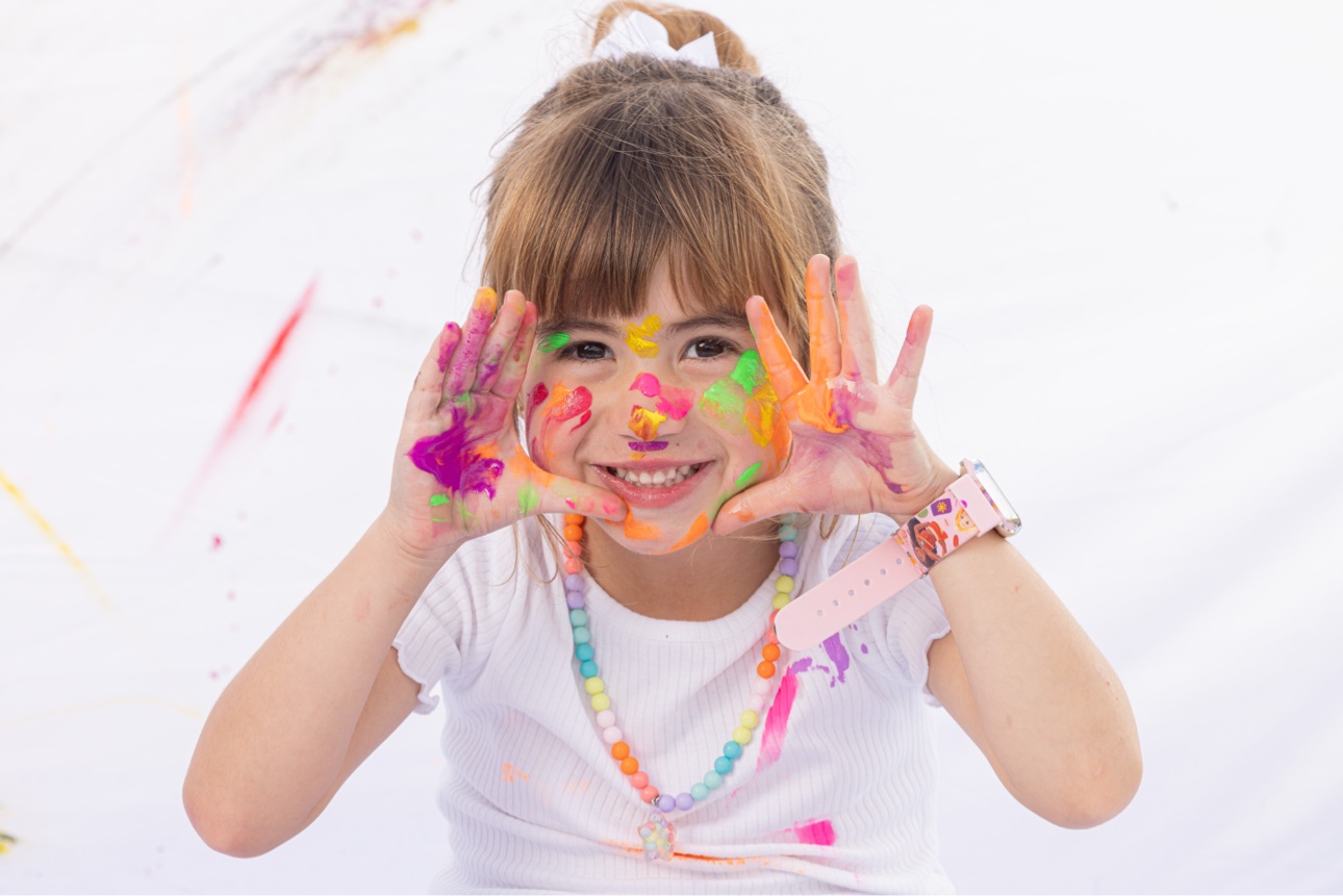 Niña sonriendo con la cara y las manos llenas de pintura de colores en su Paint Day Party